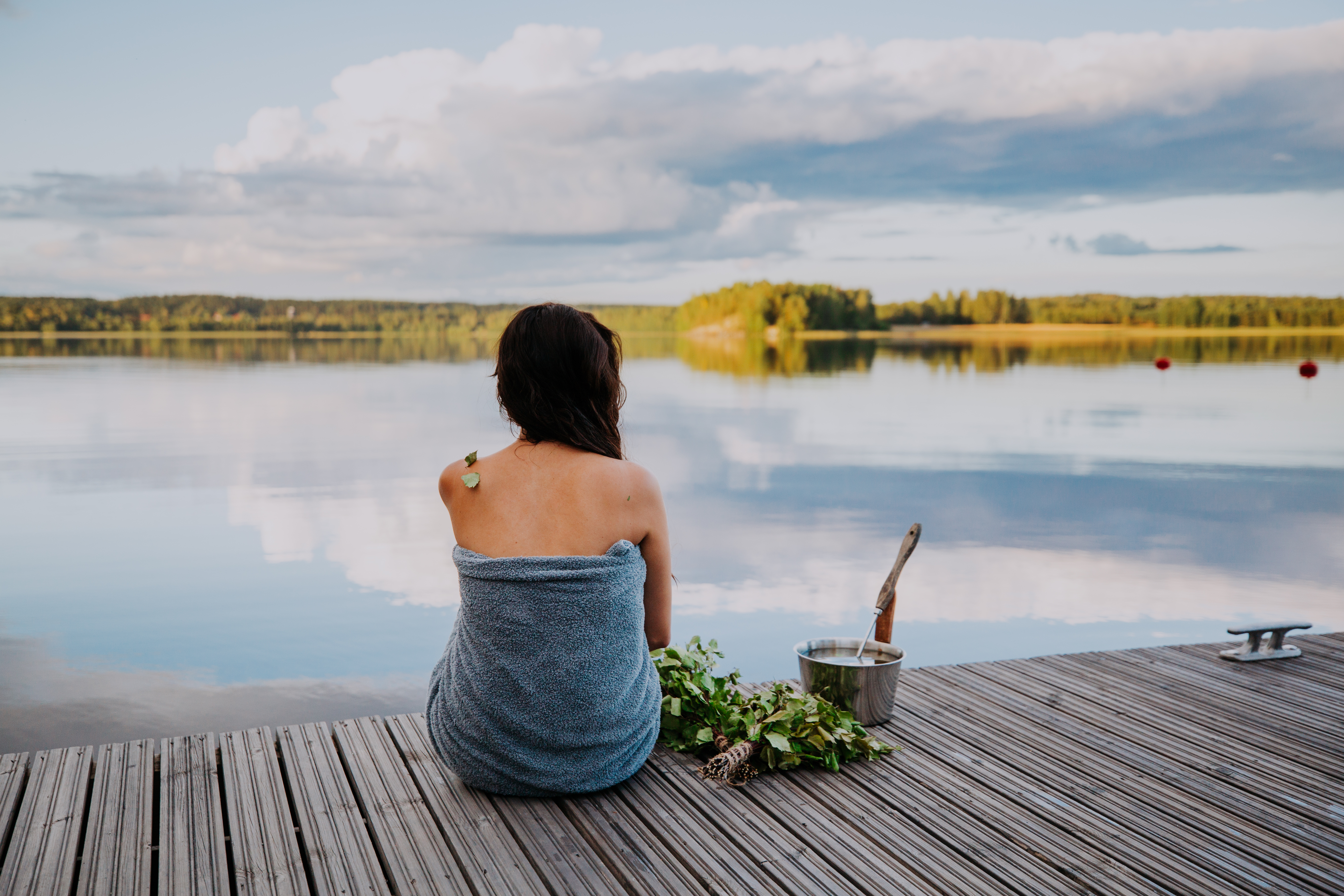 donna seduta su un molo che ammira un lago prima di andare in una sauna
