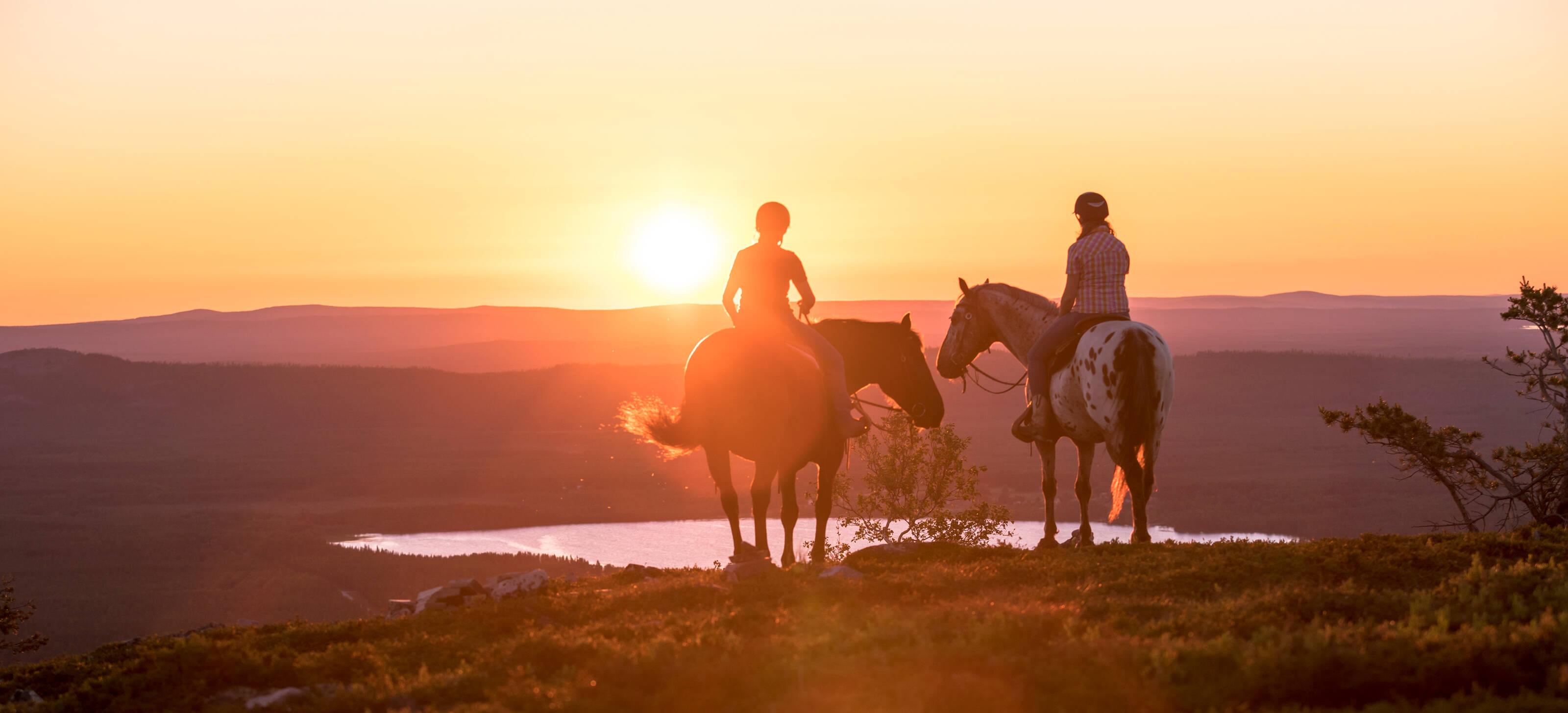 dos jinetes con sus caballos mirando al Sol de Medianoche
