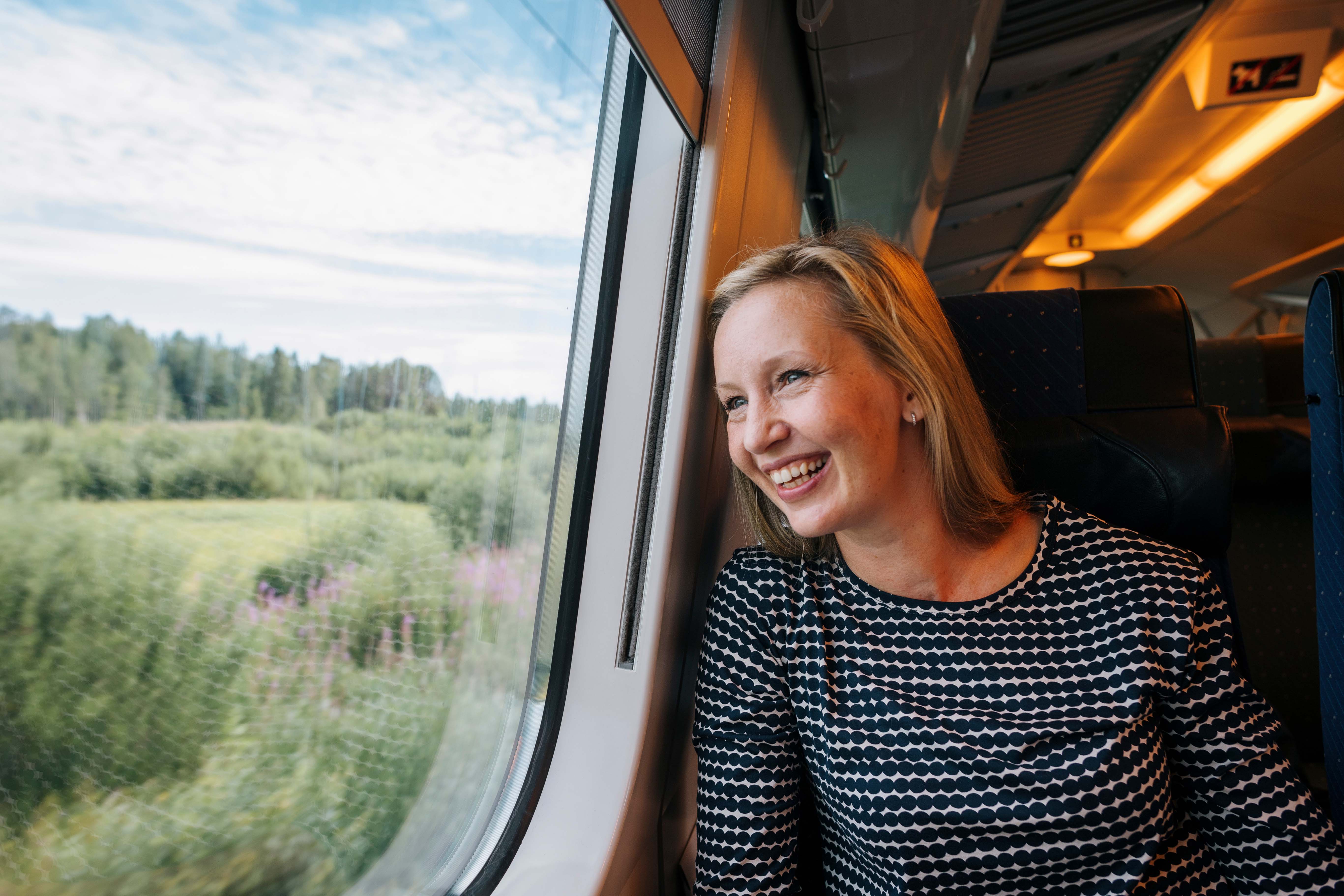 A happy traveller looking out of a train window at a green Finnish countryside.