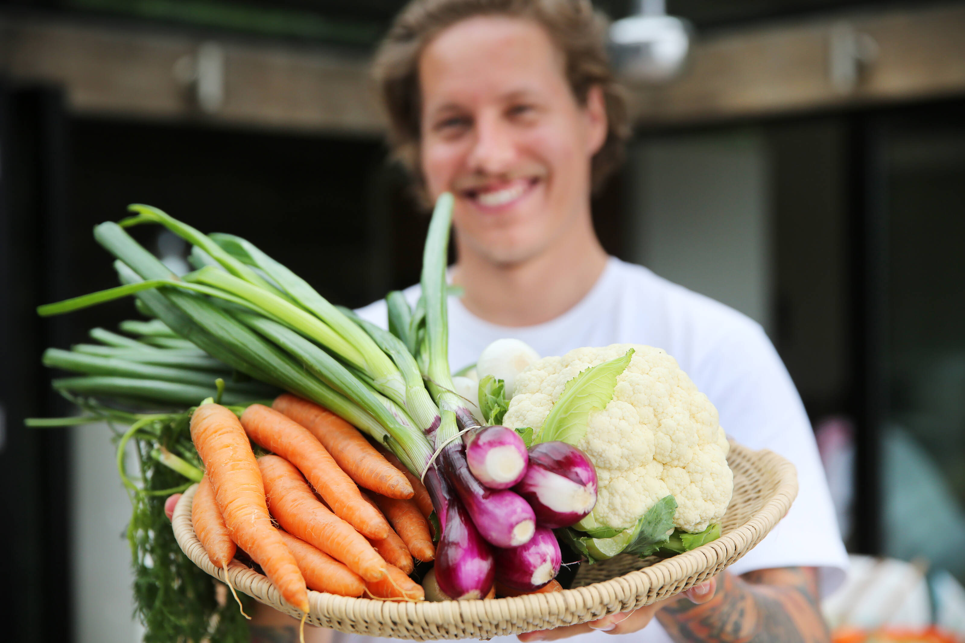 a man is holding a weaved tray full of fresh Finnish vegetables