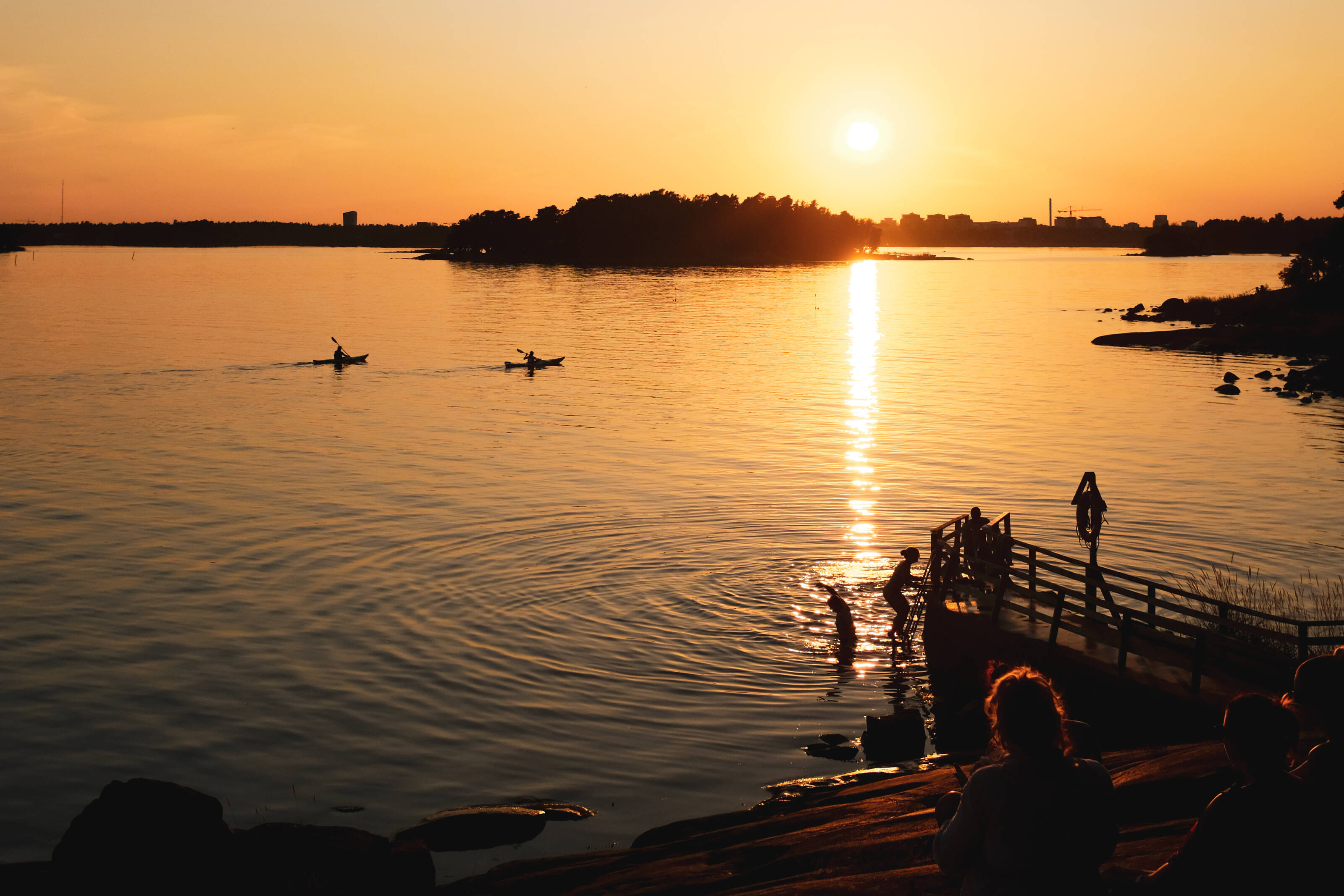 真夜中の太陽に照らされたヘルシンキ沿岸のバルト海で泳ぐ人たち