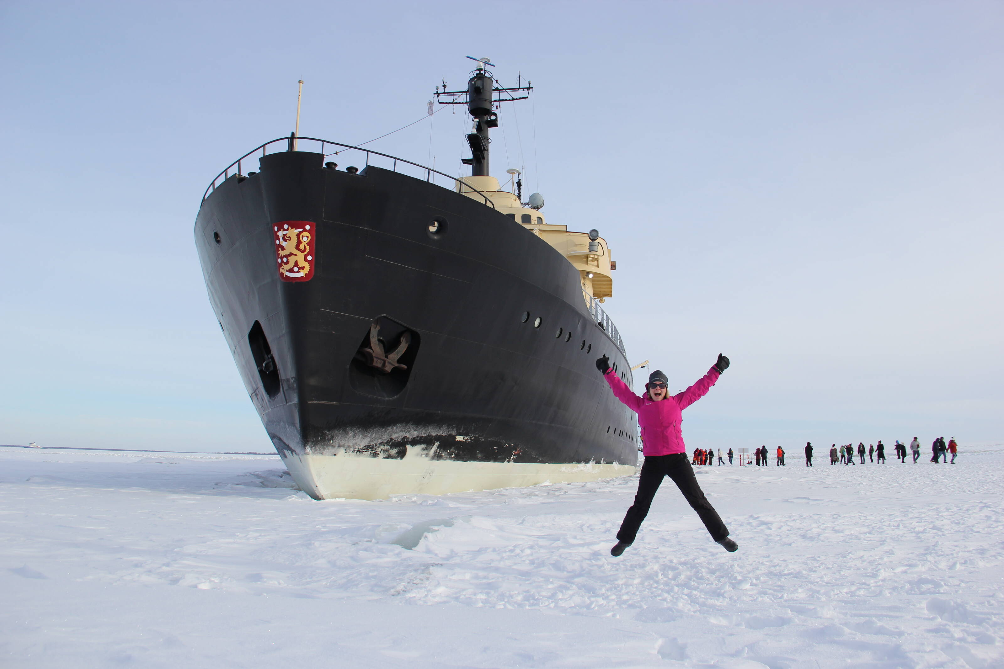 Frau, die vor dem Bug eines großen arktischen Eisbrechers in die Luft springt
