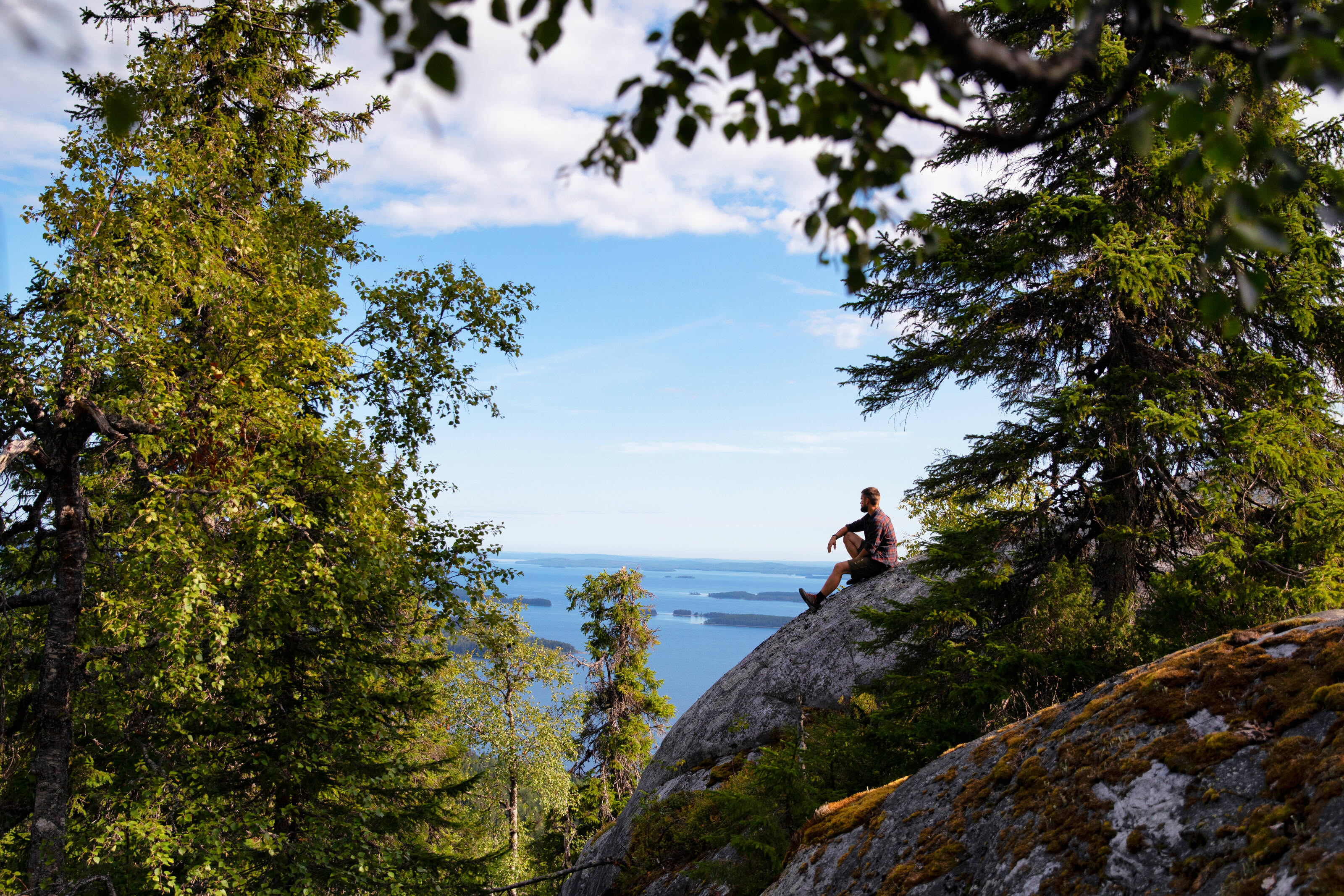 Мужчина сидит на скале у озера в Финляндии