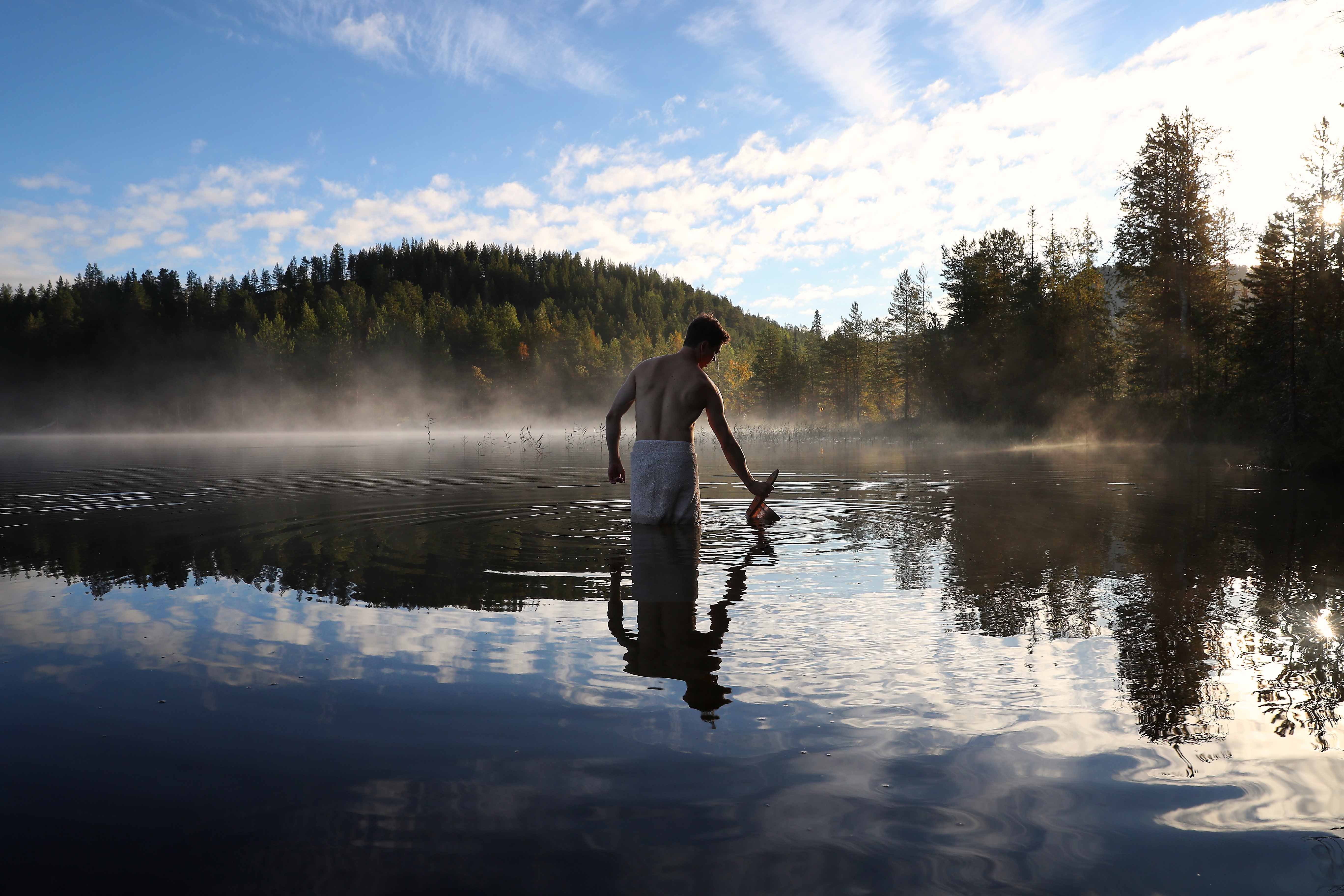 a man standing in a lake while filling sauna pail