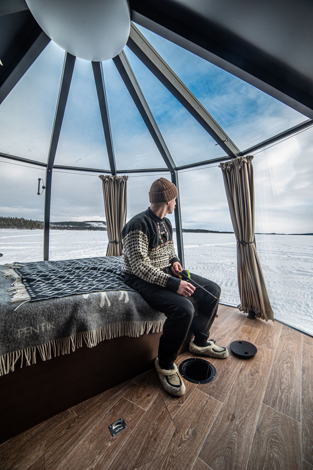 A person ice fishing inside a glass cabin