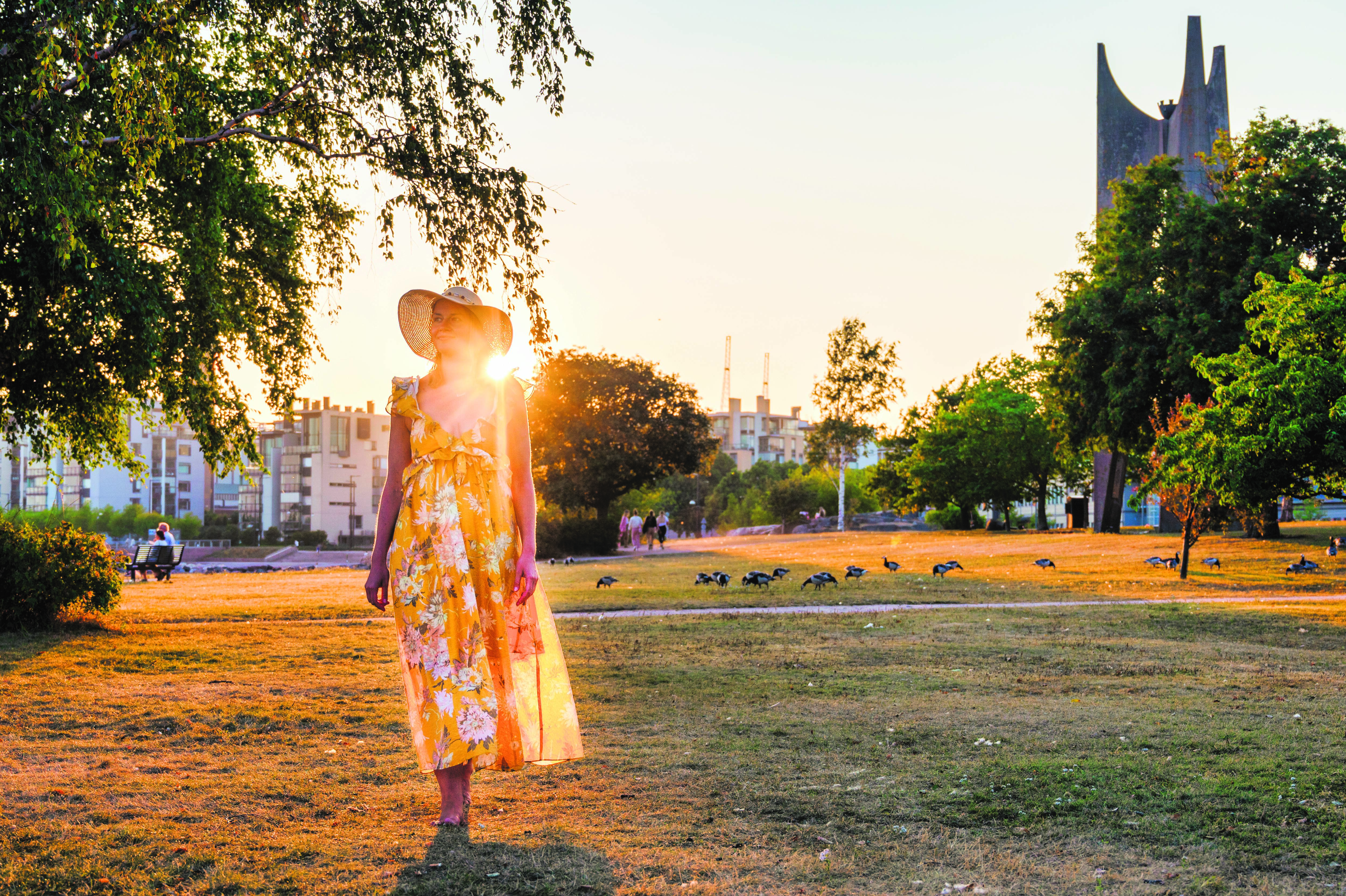 Frau im Sommerkleid, die unter der Mitternachtssonne in einem Park spazieren geht