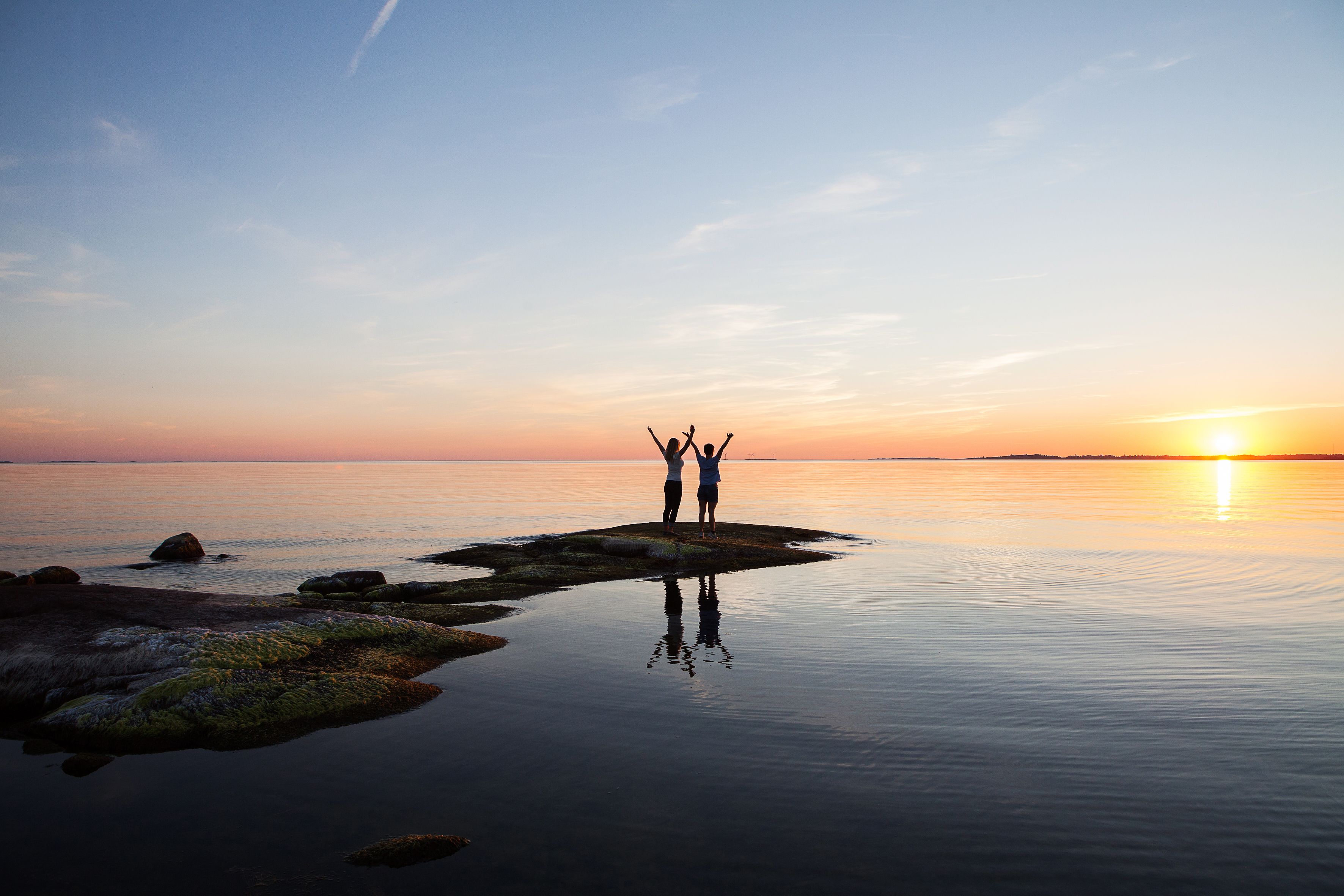 Deux personnes saluent le soleil sur un rivage d’Åland