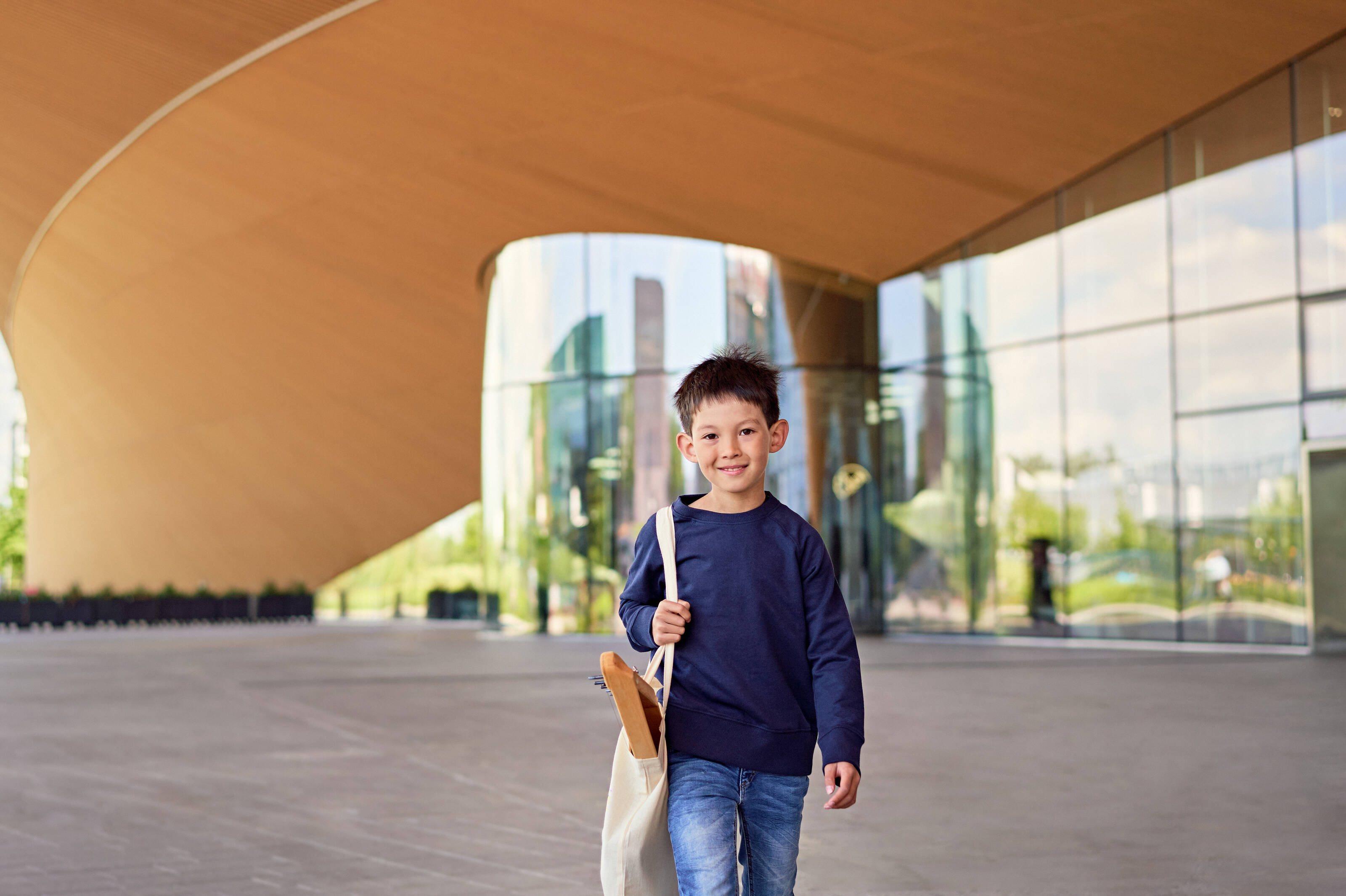 A young boy carrying a kantele walking out of the Oodi library in Helsinki