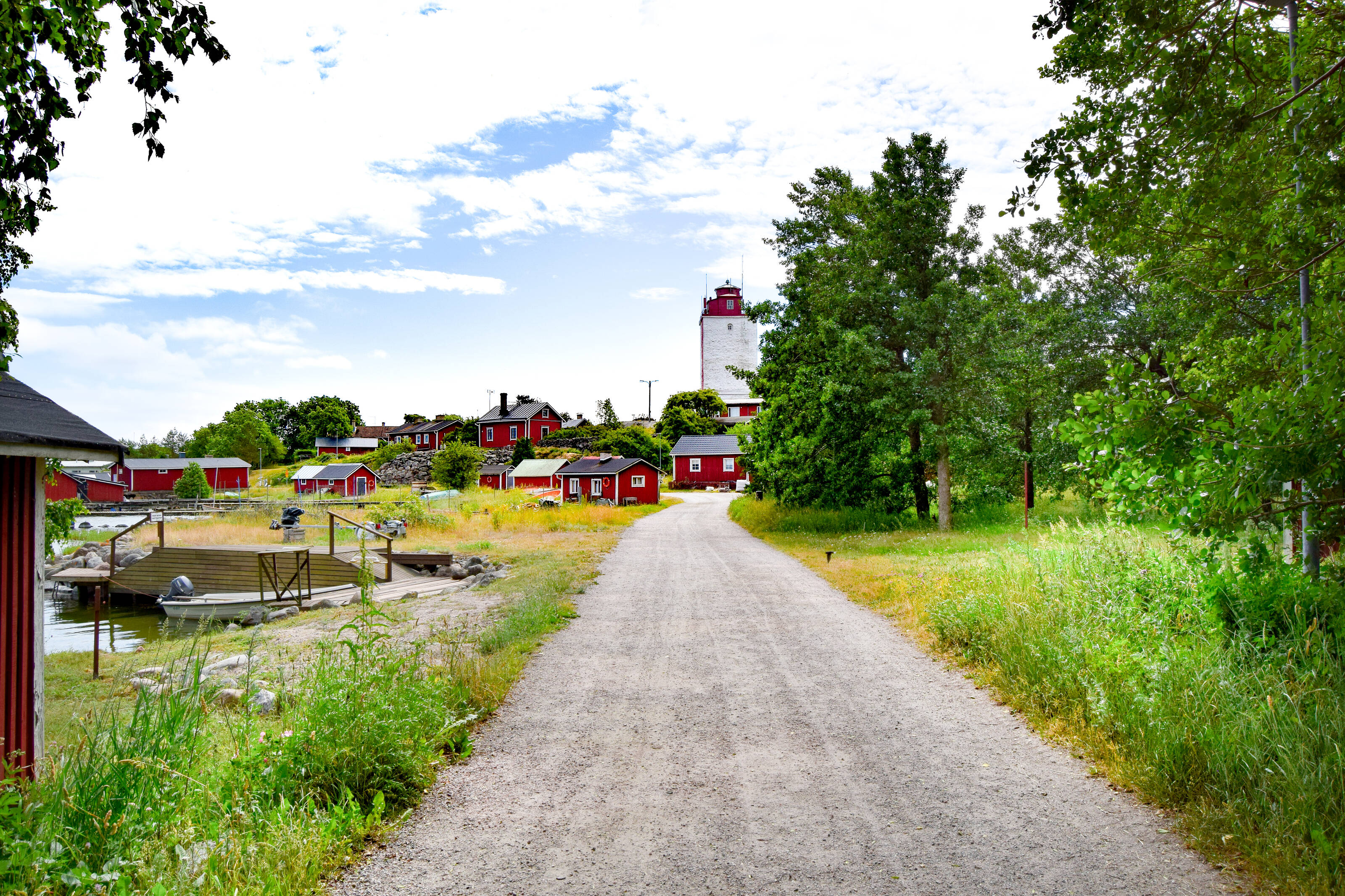 Eine Schotterstraße führt zu einem idyllischen Dorf voller roter Holzhäuser mit dem roten Leuchtturm Utö in der Mitte