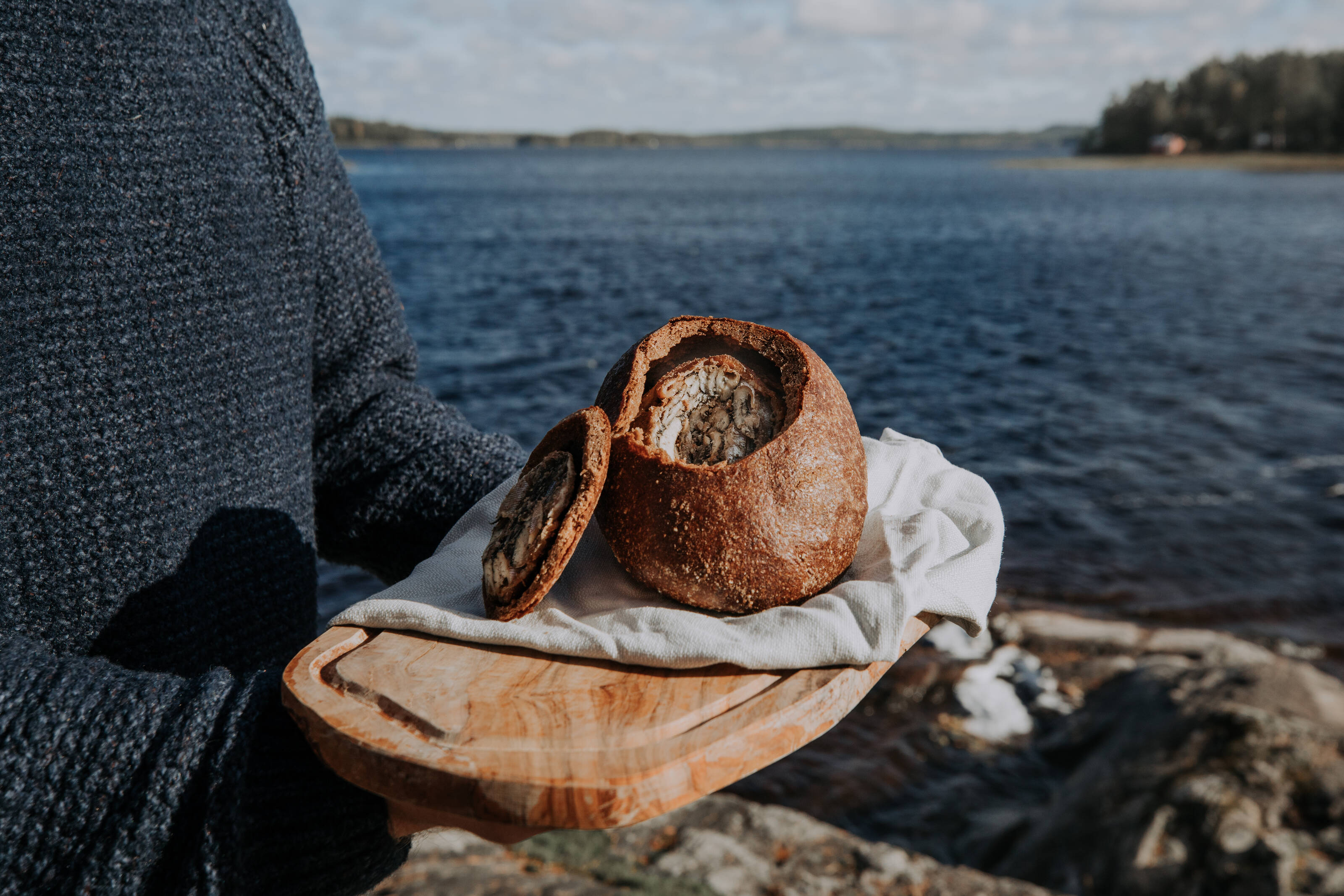 una persona junto a un lago con un kalakukko, uno de los alimentos icónicos de Savo