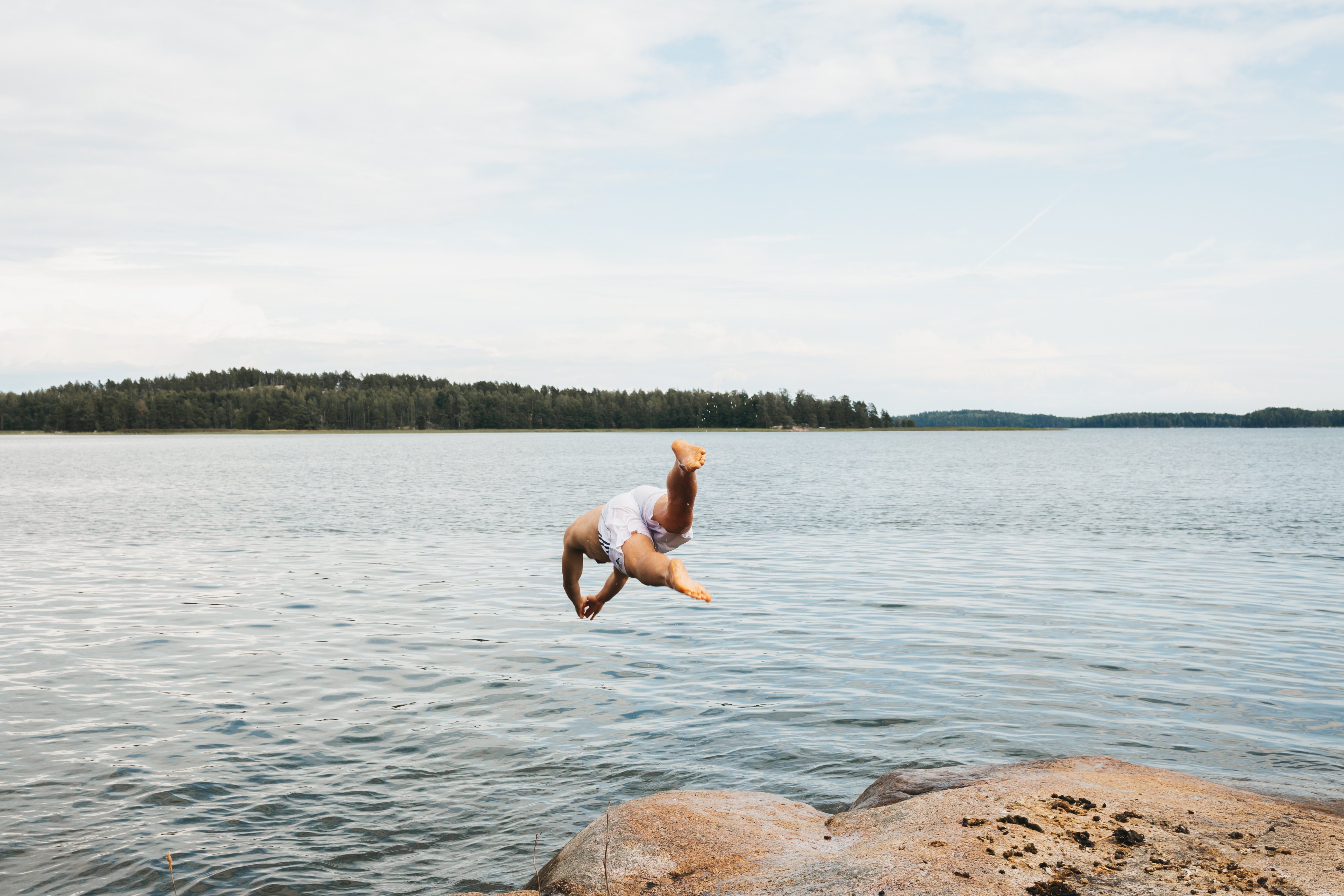 a man jumping from a small cliff into the water