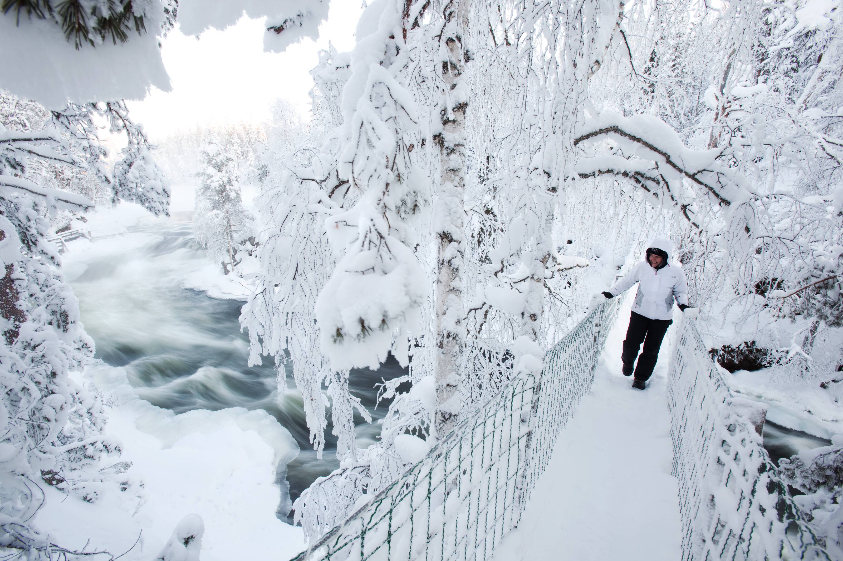 Frau auf einer Brücke, die über verschneite Stromschnellen führt